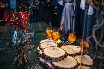 Drink setup features vibrant cocktails with orange slices on rustic wooden platters. Flowers and elegant decor create a sophisticated atmosphere at a social gathering.