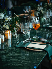 Elegant table setting featuring crystal glassware, a cocktail, floral arrangements, and candles on a dark marble surface, perfect for a formal dining experience.