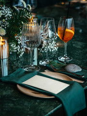 Formal dining table elegantly set with a wine glass, cocktail glass, plates, and green napkins. Florals and candles add a sophisticated touch, perfect for a fine dining experience.