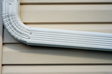 Closeup of an new downspout as it bends along the side of a house with newly installed vinyl siding