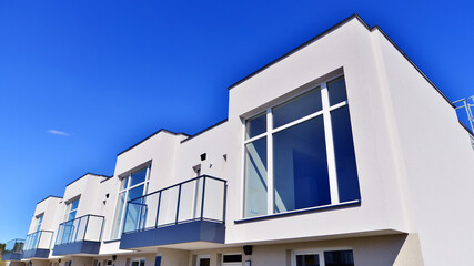 Terraced family homes in newly developed housing estate. The real estate market in the suburbs. New single family houses in a new development area. Residential homes with modern facade. 