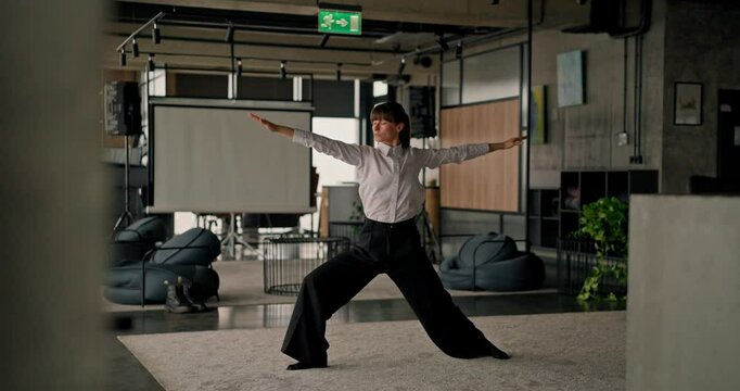 Caucasian female office worker performs yoga and stretching on a grey carpet in a modern office taking care of her physical health