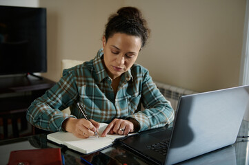 Woman Writing and Using Laptop in a Home Office Setting