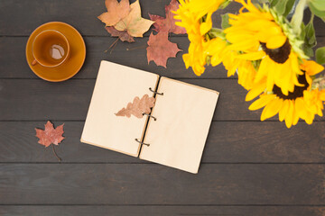 Open notebook with bouquet of sunflowers and empty brown cup on wooden table