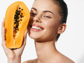 Smiling woman holding fresh papaya in front of face, tropical fruit concept for healthy eating and natural skincare advertising