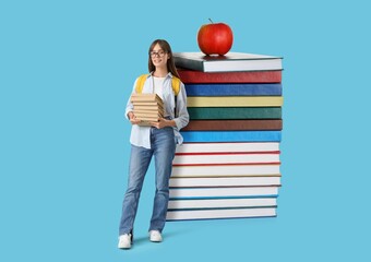 Happy female student with many big books on light blue background
