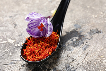 Spoon with dried saffron threads and crocus flower on grey grunge table