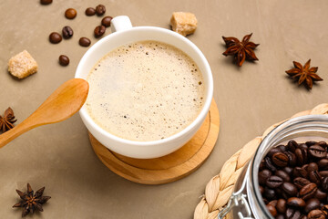 Cup of hot espresso and jar with coffee beans on brown background
