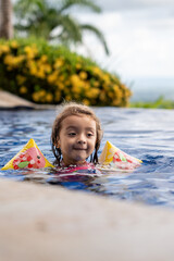 A child joyfully swims in a vibrant pool with floaties, enjoying the warm sunshine