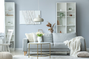 Cozy grey sofa with soft blanket and table in interior of light living room