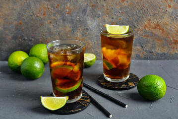 Glasses of cold Cuba Libre cocktail and limes on grey table