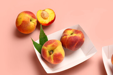 Paper plate with sweet peaches and leaves on pink background