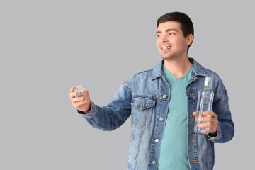 Young man with glass and bottle of vodka on light background