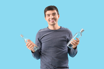 Young man with bottles of vodka on blue background