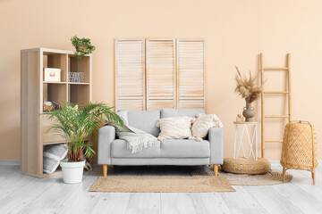 Naklejka premium Interior of light living room with stylish grey sofa, shelving unit, folding screen and ladder