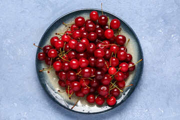 Plate with red sweet cherries on blue background