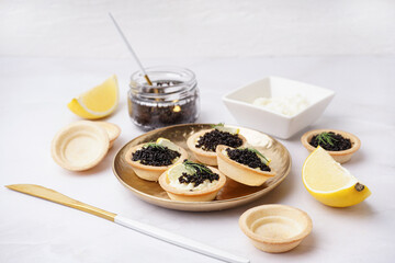 Plate of tasty tartlets with black caviar on grey background
