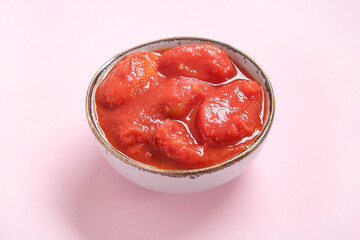 Bowl of tasty canned tomatoes on pink background