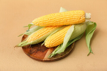 Wooden board with fresh corn cobs on brown background