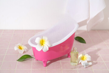 Small bathtub with foam, bottle of essential oil and tropical flowers on color tile table