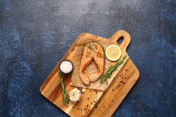 Wooden board of tasty salmon steak with lemon and garlic on blue background