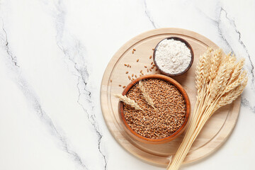 Wooden bowls of grains and flour with wheat ears on grunge white background