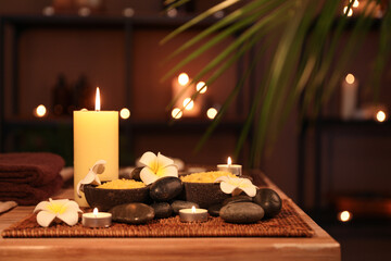 Spa composition with plumeria flowers and burning candles on table in dark salon, closeup