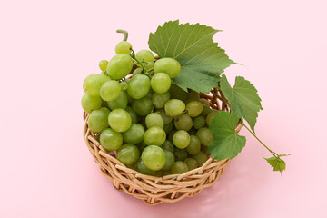 Wicker bowl with sweet green grapes and leaves on pink background