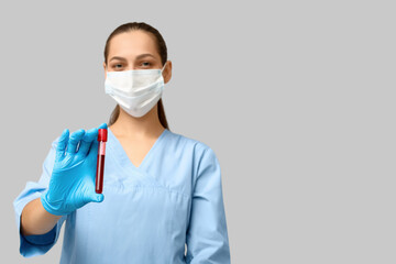 Portrait of female doctor in mask holding test tube with blood sample on grey background