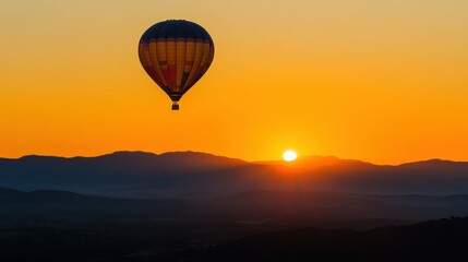 Naklejka premium Hot air balloon floats over silhouetted mountains at sunrise. Golden landscape.