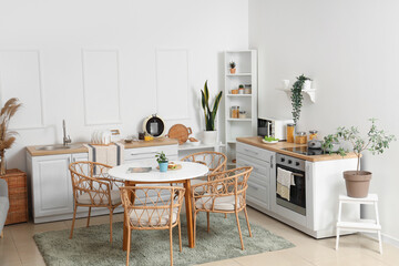 Interior of light kitchen with green plants, counters and dining table