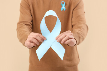 Young man with blue ribbons on beige background, closeup. Prostate cancer awareness concept