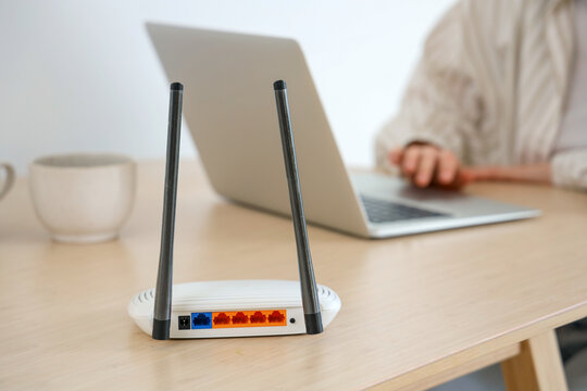 Modern wi-fi router on table of woman using laptop in room, closeup