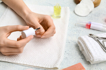 Female hands with bottle of cuticle oil, towel and cutter on light background