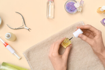 Female hands holding bottle of cuticle oil with towel, cutter and sea salt on beige background