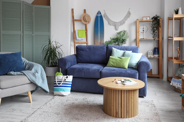 Interior of light living room with blue sofa, surfboard and coffee table