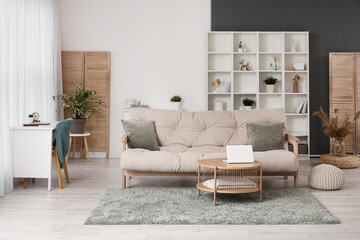 Interior of light living room with cozy sofa, coffee table and shelving unit