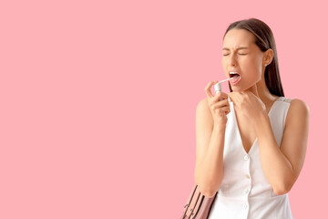 Young woman using spray for sore throat on pink background
