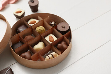 Box with delicious chocolate candies on white wooden background, closeup