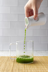 Chef pouring matcha tea into glass cup in modern kitchen