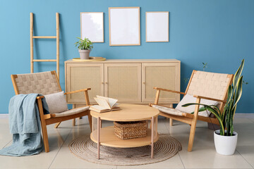 Comfortable armchairs, coffee table and chest of drawers near blue wall in room