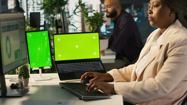 Isolated screen laptop and tablet on office desk next to employee editing documents on computer. Chroma key devices next to worker analyzing data charts, interpreting statistical information, camera A