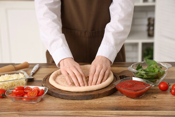 Woman preparing dough for pizza near table in kitchen