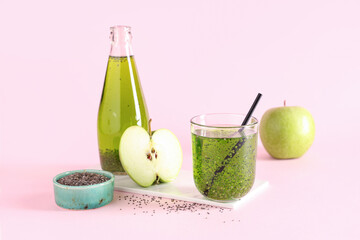 Bottle and glass of lemonade with chia seeds and apples on pink background