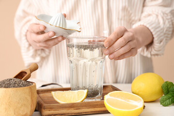 Woman adding lemon juice into glass of water with chia seeds near table
