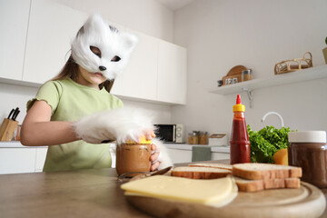 Quadrober girl in cat disguise preparing peanut sandwich in kitchen