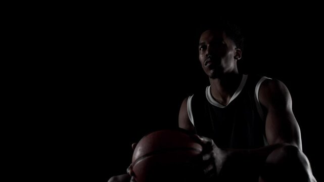 Basketball player sitting on a bench. Looking forward. Concentrated african american sports man against black background.