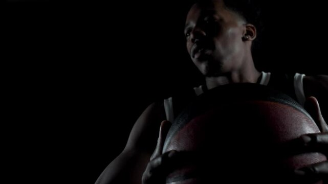 Basketball player sitting on a bench taking deep breath in and looking down. Concentrated african american man against black background.