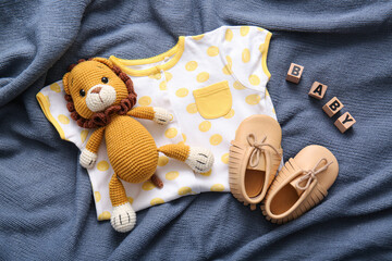 Toy lion, baby bodysuit and booties on dark fabric background