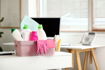 Plastic basket with cleaning supplies on table in modern office, closeup